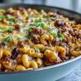 A hearty One-Pan High Protein Chili Mac with beans and pasta in a skillet, topped with green onions and sour cream.