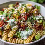 Vibrant Tex-Mex Easy Taco Pasta Salad loaded with avocado, bell peppers, and cheddar cheese, topped with crushed tortilla chips.  