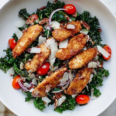A hearty American dinner salad features crunchy panko-breaded chicken, massaged kale, and colorful vegetables, drizzled with sweet and tangy maple-Dijon vinaigrette.