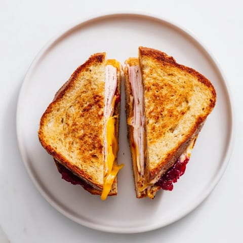 A close-up of Smoked Turkey Grilled Cheese with gooey cheddar and cranberry spread, served alongside sweet potato fries.  