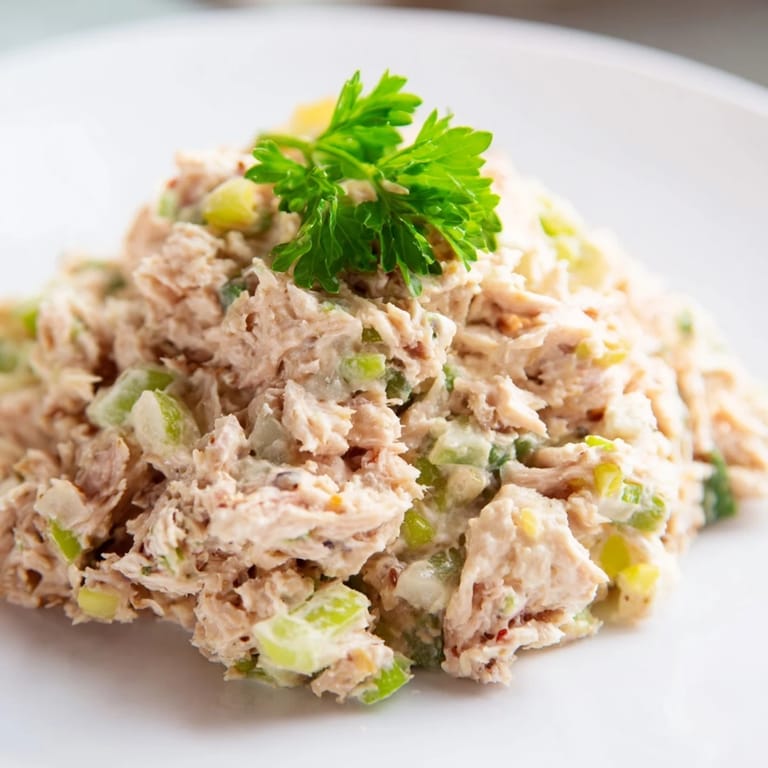A fresh spicy zesty tuna salad in a glass jar with lemon wedges and herbs, ready for a picnic or quick lunch.