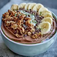 Two bowls of Chunky Monkey smoothie bowls topped with sliced bananas, crunchy granola, cacao nibs, and hemp seeds.