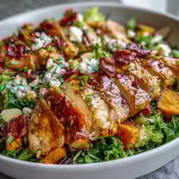 A plated Harvest Bowl with roasted sweet potatoes, sliced chicken, kale, apples, and goat cheese, drizzled with balsamic dressing.