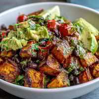 A bowl of Sweet Potato and Black Bean Bowl with roasted sweet potatoes, black beans, fresh avocado, and zesty lime dressing over greens.